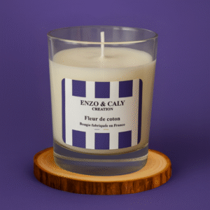 Bougie parfumée senteur Fleur de coton, présentée dans un verre transparent avec étiquette mauve et blanche, posée sur un rondin en bois et sur un fond uni mauve – création élégante Enzo & Caly fabriquée en France.