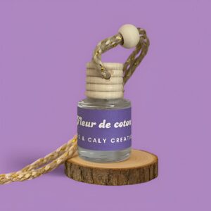 Mini diffuseur au parfum Fleur de coton, présenté dans un petit flacon en verre transparent, avec une étiquette mauve et un cordon torsadé, posé sur un rondin en bois avec un fond uni mauve – création élégante Enzo & Caly fabriquée en France.