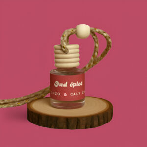 Mini diffuseur au parfum Oud épicé, présenté dans un petit flacon en verre transparent, avec une étiquette rouge et un cordon torsadé, posé sur un rondin en bois avec un fond uni rougeâtre – création élégante Enzo & Caly fabriquée en France.