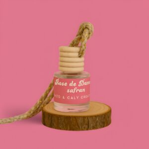 Mini diffuseur au parfum Rose Damas safran, présenté dans un petit flacon en verre transparent, avec une étiquette rose et un cordon torsadé, posé sur un rondin en bois avec un fond uni rose – création élégante Enzo & Caly fabriquée en France.