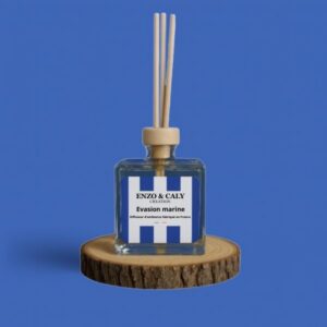 Diffuseur d’ambiance au parfum Evasion marine, à tiges en bois, présenté dans un flacon carré en verre transparent, avec une étiquette bleue et blanche, posé sur un rondin en bois avec un fond uni bleu– création élégante Enzo & Caly fabriquée en France.