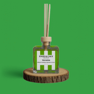 Diffuseur d’ambiance au parfum Verveine, à tiges en bois, présenté dans un flacon carré en verre transparent, avec une étiquette verte et blanche, posé sur un rondin en bois avec un fond uni vert – création élégante Enzo & Caly fabriquée en France.