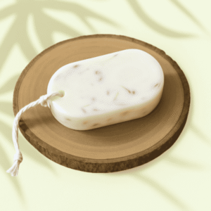 tablette parfumée au bouquet poudré, René et Gigi, de forme ovale , de couleur crème et marbrée de fleurs et feuilles séchées, avec une cordelette blanche, posée sur une tranche de bois en décor naturel.