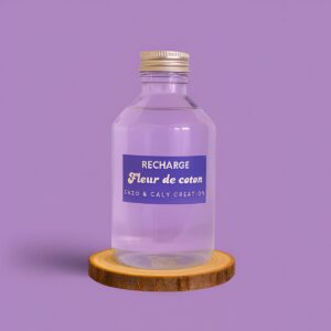 Recharge de parfum d’ambiance Fleur de coton, présentée dans une bouteille en verre transparent avec étiquette mauve, posée sur un rondin en bois et un fond uni mauve – création élégante Enzo & Caly fabriquée en France.