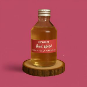Recharge de parfum d’ambiance au Oud épicé, présentée dans une bouteille en verre transparent avec étiquette rouge, posée sur un rondin en bois et un fond uni rougeâtre – création élégante Enzo & Caly fabriquée en France.