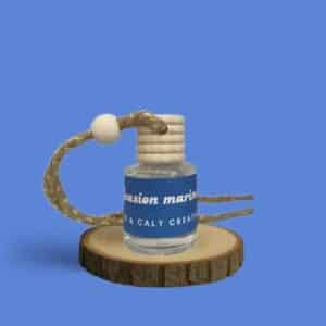 Mini diffuseur au parfum Evasion Marine, présenté dans un petit flacon en verre transparent, avec une étiquette bleue et un cordon torsadé, posé sur un rondin en bois avec un fond uni bleu – création élégante Enzo & Caly fabriquée en France.