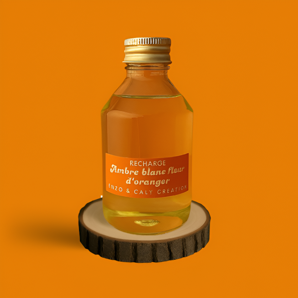 Recharge de parfum d’ambiance Ambre blanc fleur d'oranger, présentée dans une bouteille en verre transparent avec étiquette orange, posée sur un rondin en bois et un fond uni orange – création élégante Enzo & Caly fabriquée en France.