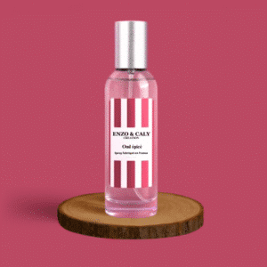 Spray au parfum d’ambiance Oud épicé, présenté dans une bouteille en verre transparent avec une étiquette bordeaux et blanche, posé sur un rondin en bois avec un fond uni bordeaux – création élégante Enzo & Caly fabriquée en France.